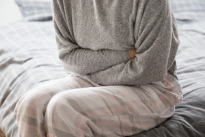 Individu se tenant le ventre, bras croisés, assis sur un lit. 
Signification : un mal de ventre 