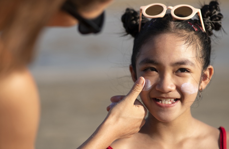 image d'une fille se faisant appliquer de la crème solaire sur les joues