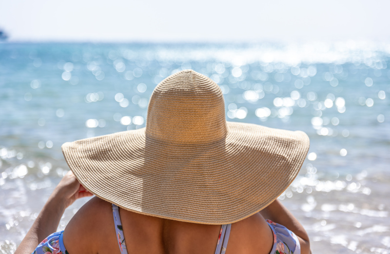 Une femme avec un grand chapeau à bords large sur la plage proche de la mer